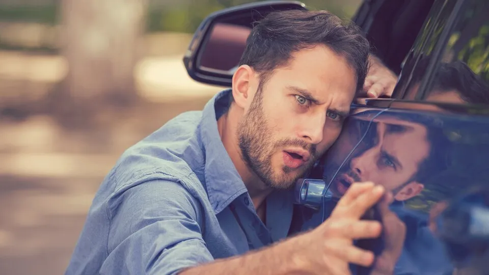 Young worried funny looking man obsessing about cleanliness of his new car on a summer day. Car care and protection concept